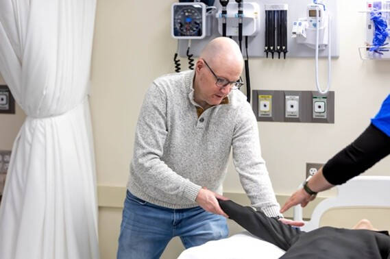 A faculty member demonstrates a technique on a manikin in a simulated hospital setting